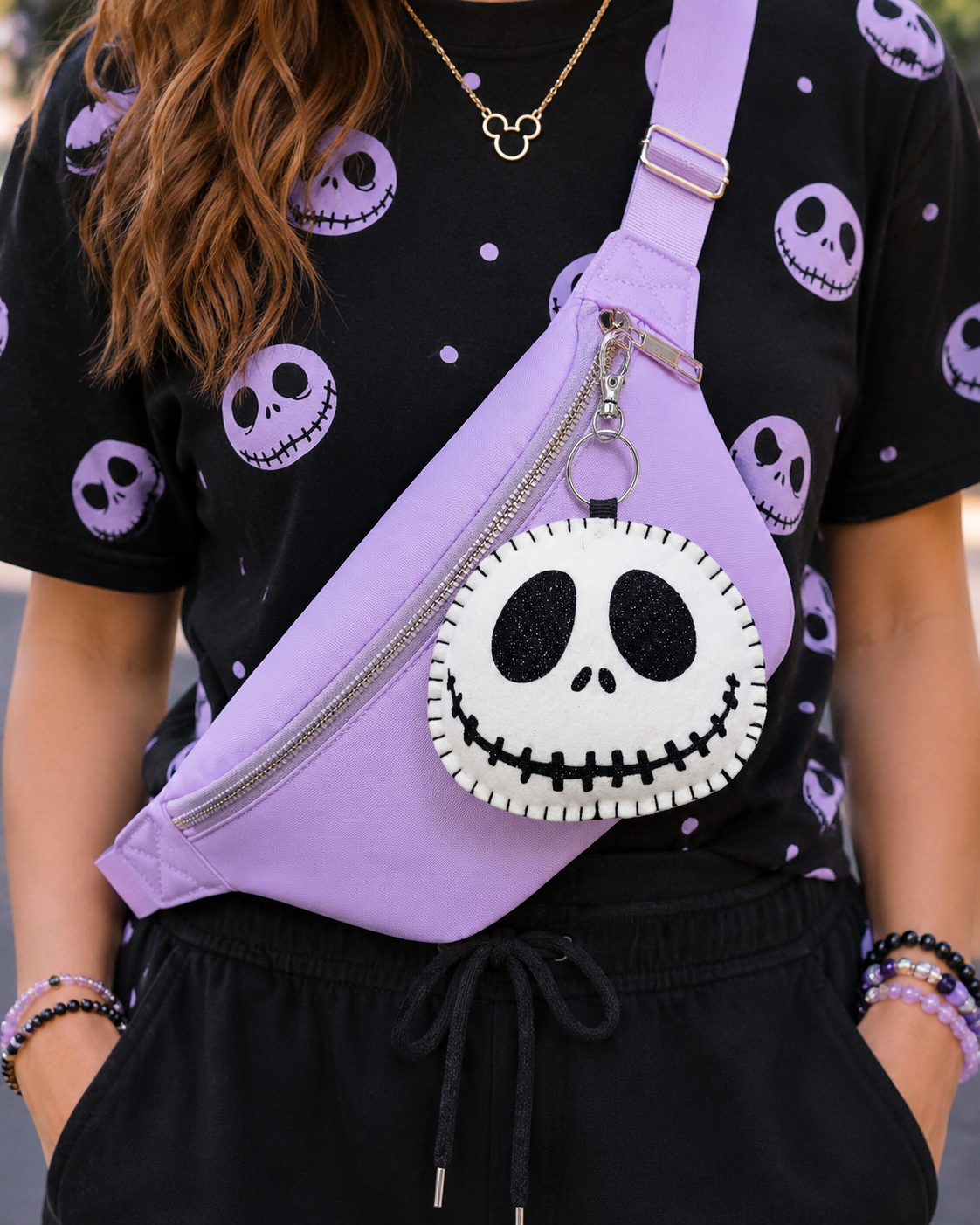 A person wearing a black t-shirt and black sweatpants with a purple Disney-themed crossbody bag featuring a Jack Skellington skull charm.